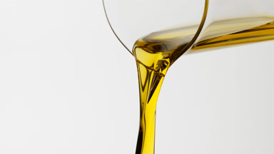 Sunflower oil is being poured from beaker on grey background