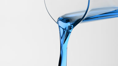 Macro of blue oil is being poured from beaker on grey background