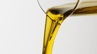 Olive oil is being poured from beaker on grey background