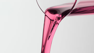 Macro of rosehip oil being poured from beaker on grey background