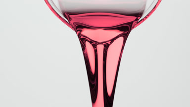 Macro of pink liquid being poured from beaker on grey background