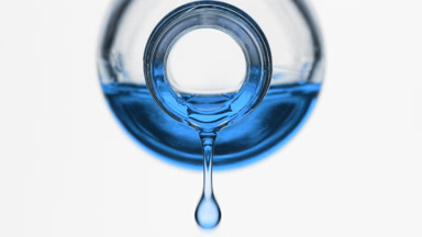 Blue oil is dripping from reagent bottle on grey background
