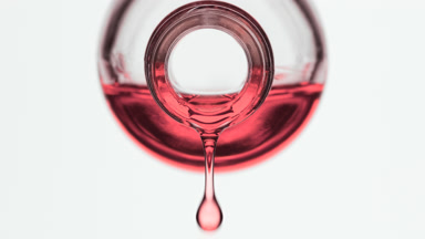 Pink oil is dripping from reagent bottle on grey background