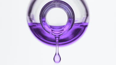 Purple oil is dripping from reagent bottle on grey background