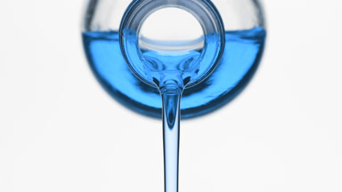Cyan oil is being poured from reagent bottle on grey background