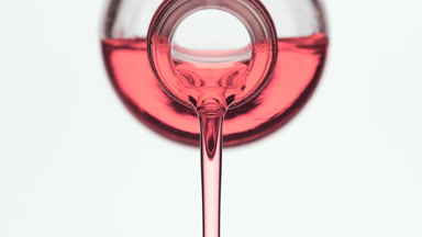 Rose oil is being poured from reagent bottle on grey background