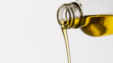 Yellow oil being poured from reagent bottle on white background