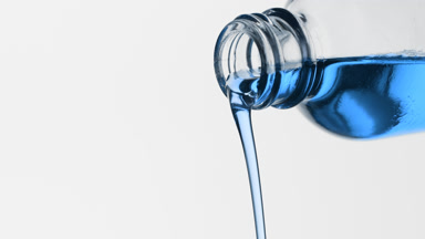 Blue oil is being poured from reagent bottle on grey background