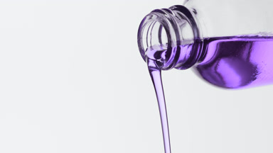 Purple oil being poured from reagent bottle on grey background