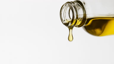 Yellow oil is dripping from reagent bottle on white background