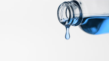 Cyan oil is dripping from reagent bottle on grey background