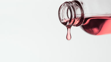 Rose oil is dripping from reagent bottle on grey background