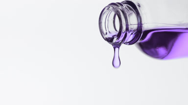 Violet oil is dripping from reagent bottle on grey background