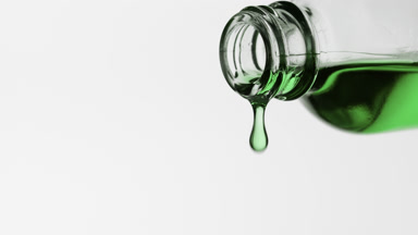 Avocado oil is dripping from reagent bottle on grey background