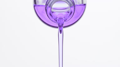 Lavender oil being poured from reagent bottle on grey background