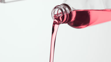 Reagent bottle is being tilted and pink oil pours from it
