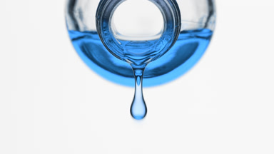 Cyan liquid is dripping from reagent bottle on grey background