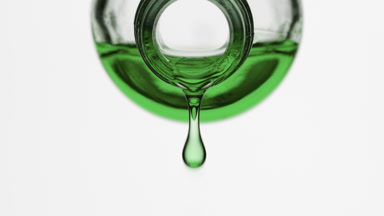 Green liquid is dripping from reagent bottle on grey background