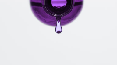 Purple liquid is dripping from purple bottle on grey background