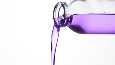 Reagent bottle is being tilted and purple fluid pours from it