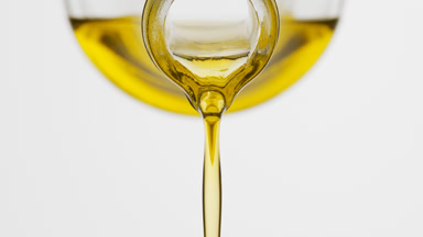 Carrot oil is being poured from conical flask on grey background