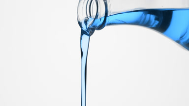 Conical flask is being tilted and cyan oil pours from it