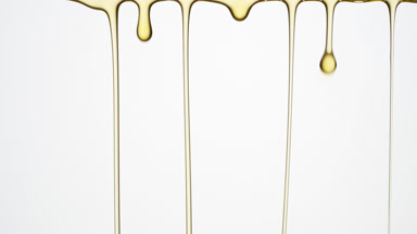 Macro of yellow oil flowing and dripping down on grey background
