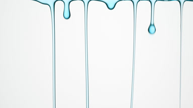 Macro of cyan oil flowing and dripping down on grey background