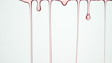 Macro of pink oil flowing and dripping down on grey background