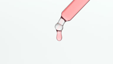 Rose water is dripping from lab dropper on grey background