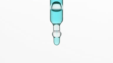 Cyan drops are falling down from lab dropper on grey background