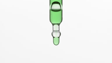 Green drops are falling down from lab dropper on grey background