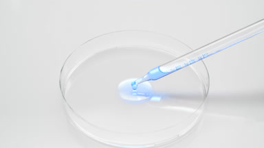 Cyan liquid dripping from long chemical dropper into Petri dish