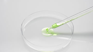 Green liquid is dripping from chemical dropper into Petri dish