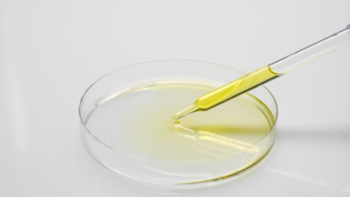 Long dropper drips yellow fluid in Petri dish and takes it back