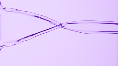 Macro of purple liquid flowing and dripping on purple background