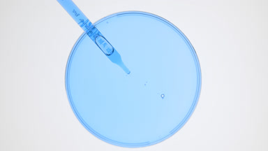 Dropper takes cyan liquid from watch glass and drips it back