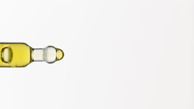 Yellow fluid is dripping from lab dropper on grey background