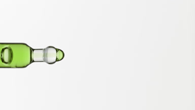 Green fluid is dripping from lab dropper on grey background