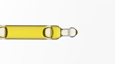 Yellow liquid is dripping from lab pipette on grey background