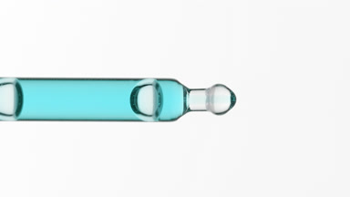 Blue liquid is dripping from lab pipette on grey background