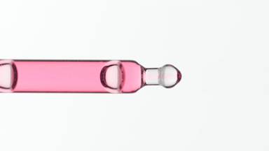 Pink liquid is dripping from lab pipette on grey background