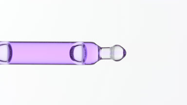 Purple liquid is dripping from lab pipette on grey background