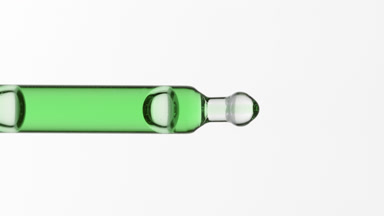 Green liquid is dripping from lab pipette on grey background