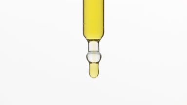 Chamomile oil is dripping from lab dropper on grey background
