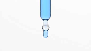 Blue tansy oil is dripping from lab dropper on grey background