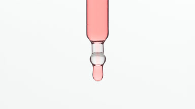Rose oil is dripping from lab dropper on grey background