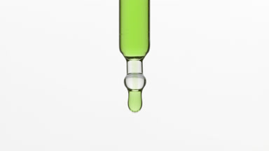 Green tea oil is dripping from lab dropper on grey background