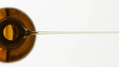 Sesame oil is being poured from brown bottle on grey background
