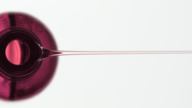 Rosehip oil is being poured from pink bottle on grey background